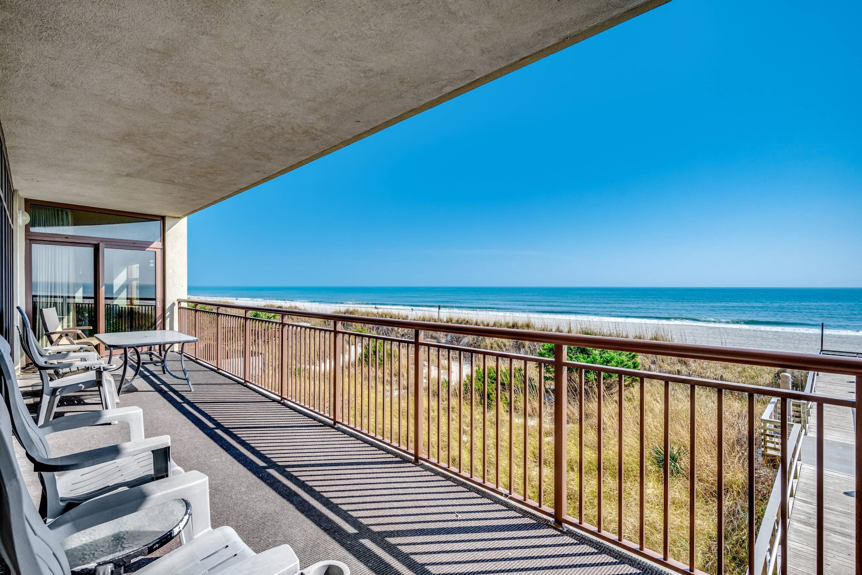 Ein Balkon mit Blick auf den Strand, ausgestattet mit Liegestühlen und einem Tisch.