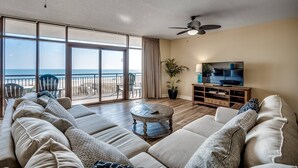 Un salon spacieux avec un grand canapé, une table basse et un téléviseur. Il y a un balcon avec vue sur l’océan.