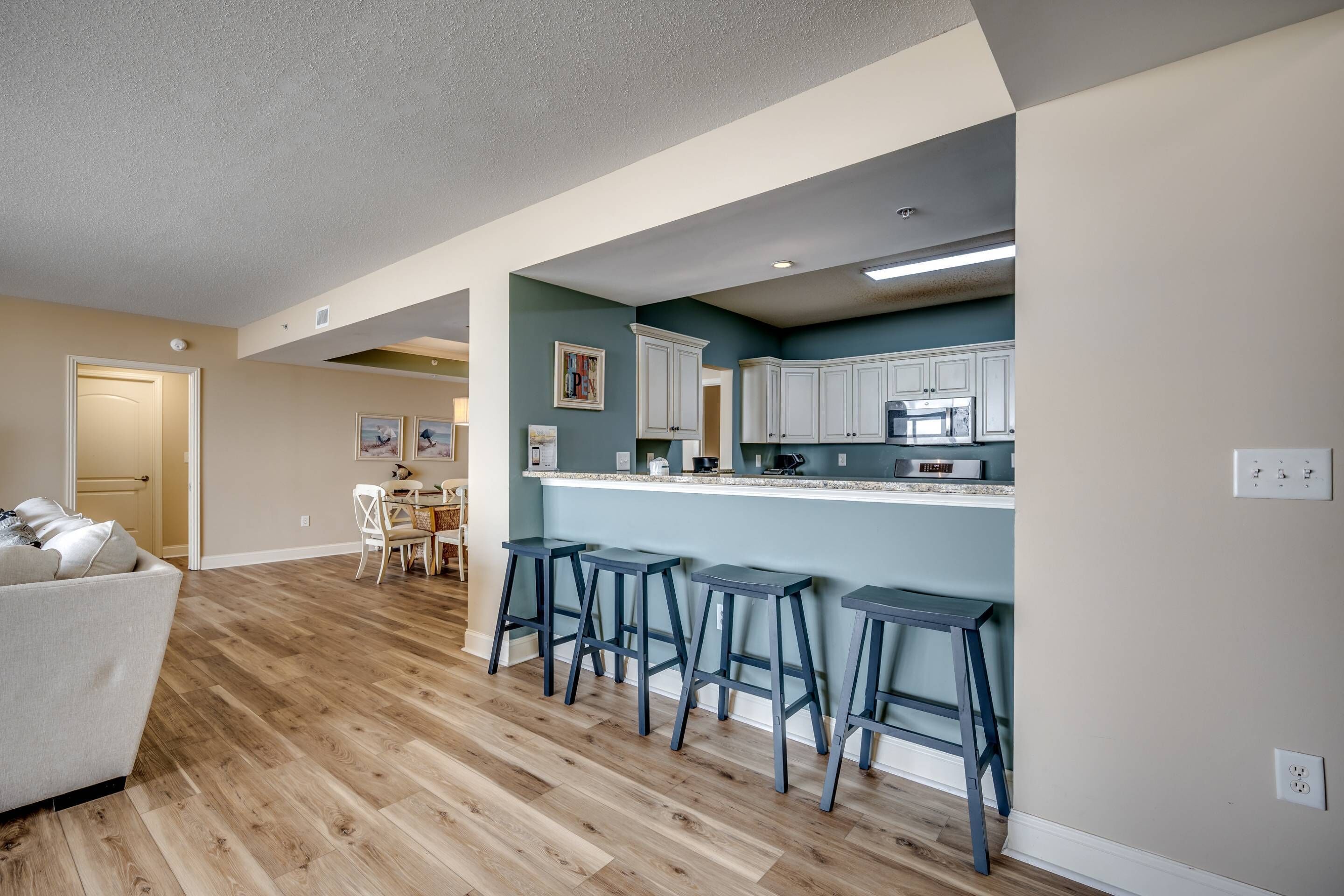 A modern kitchen with white cabinets, a bar area with stools, and a dining area with a sofa and chairs.