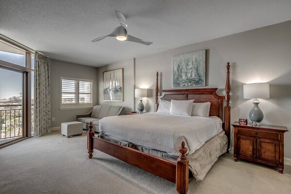 A spacious bedroom with a large bed, a ceiling fan, and a view of the city through large windows.