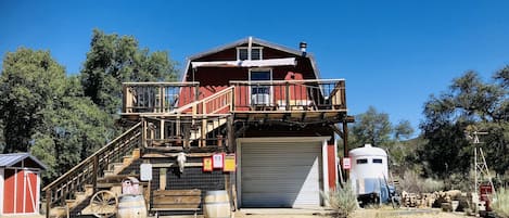 Une grange à deux étages avec un balcon, un escalier en bois et une porte de garage fermée.