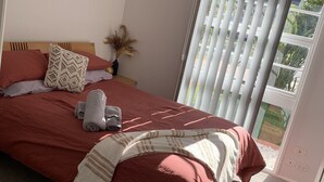 Une chambre à coucher avec un lit, un ventilateur de plafond, une fenêtre avec des stores et une porte.