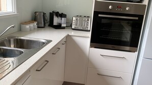 Une cuisine moderne avec des meubles blancs et des appareils en acier inoxydable, notamment un lave-vaisselle Bosch, un grille-pain Breville, un four à micro-ondes Breville et un four Valli.