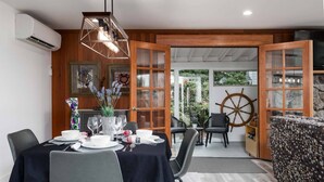 A dining area with a table set for four, chairs, a decorative vase, and a view of the garden through open doors. - *New Listing* Beautiful Riverfront Cottage, Newly Remodeled with Amazing Views, BBQ, Close to Town. (Florence)