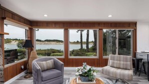 A spacious living room with a view of a lake and beach, featuring two armchairs, a coffee table, and a lamp. - *New Listing* Beautiful Riverfront Cottage, Newly Remodeled with Amazing Views, BBQ, Close to Town. (Florence)