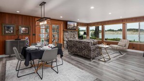 A dining area with a table set for four, a sofa, and a view of a lake. - *New Listing* Beautiful Riverfront Cottage, Newly Remodeled with Amazing Views, BBQ, Close to Town. (Florence)