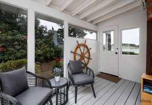 A covered porch with wicker chairs, a ship's wheel decoration, and a view of the outdoors. - *New Listing* Beautiful Riverfront Cottage, Newly Remodeled with Amazing Views, BBQ, Close to Town. (Florence)