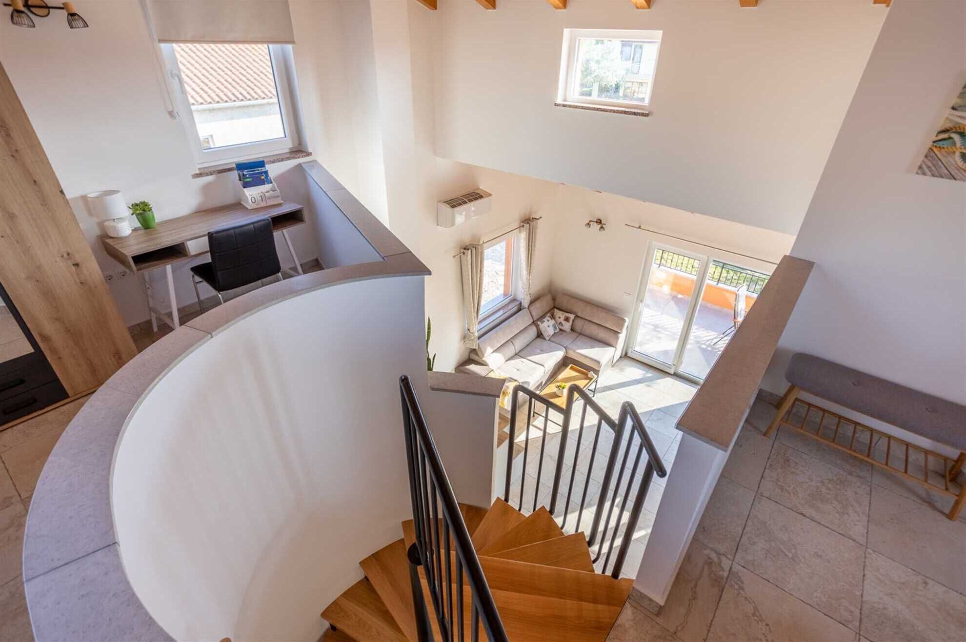A modern interior with a curved staircase, a dining area with a table and chairs, and a seating area with a sofa and a window overlooking a balcony.