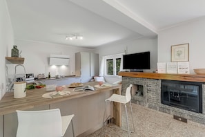 Una cocina moderna con una isla central, sillas blancas, un televisor de pantalla plana y una chimenea de piedra.