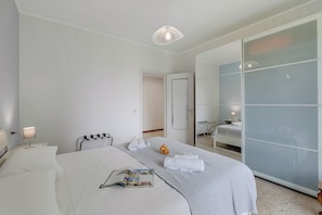Habitación de hotel moderna con una cama grande, una mesita de noche con lámpara, un espejo y un divisorio de vidrio corredero que da a un baño.