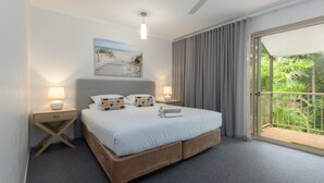 Hotellihuone, jossa on sänky, kaksi yöpöytää, pieni sivupöytä, taulu ja suuri ikkuna, josta avautuu näkymä vehreään maisemaan.