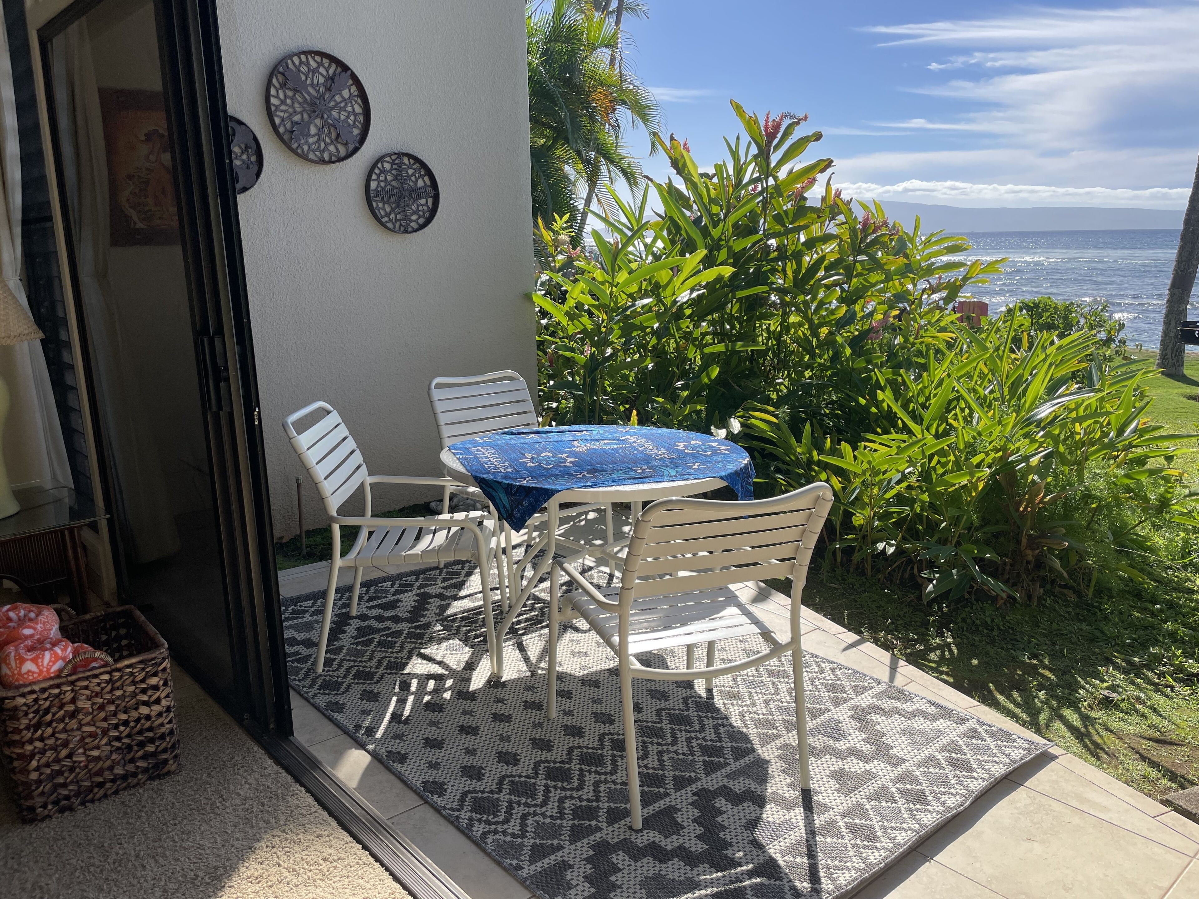 A patio with a round table and chairs, a patterned rug, and a view of the ocean.