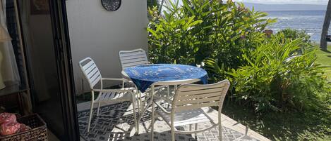 A patio with a round table and chairs, a patterned rug, and a view of the ocean.