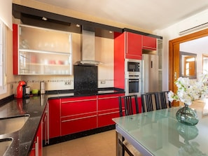A modern kitchen with red cabinetry, a glass dining table, and stainless steel appliances.