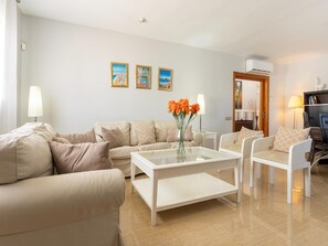 A living room with a sofa, armchairs, a coffee table, and a vase of flowers. There are three framed pictures on the wall.