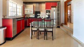 Une cuisine moderne avec des meubles de rangement rouges, une table à manger avec des chaises et un réfrigérateur.