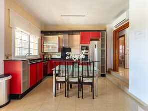 A modern kitchen with red cabinetry, a dining table with chairs, and a refrigerator.