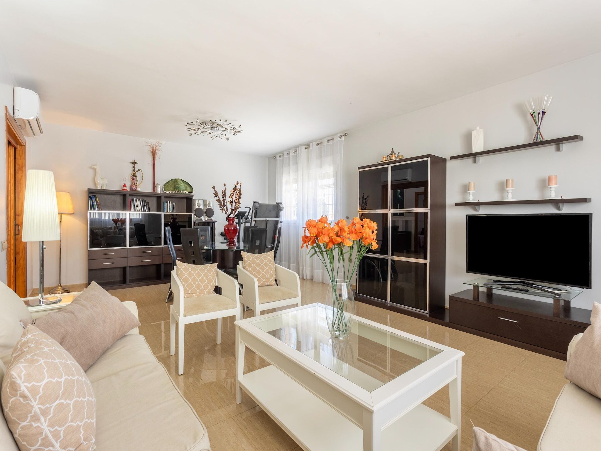A modern living room with a sofa, chairs, a coffee table, a TV, a bookshelf, and a dining area.