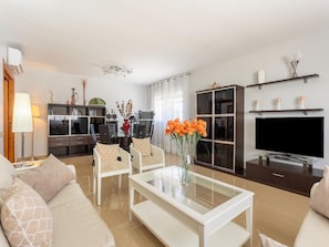 A modern living room with a sofa, chairs, a coffee table, a TV, a bookshelf, and a dining area.