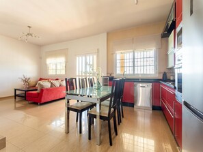 A modern kitchen with a dishwasher, red cabinets, and a dining area with a glass table and chairs.