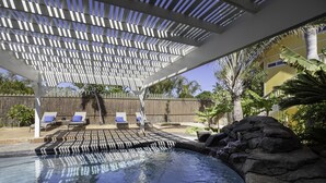 Et poolområde med pergola, liggestole og klippeformation.