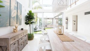 Un intérieur moderne avec une table à manger en bois, des chaises blanches, une cloison en verre et une grande plante.