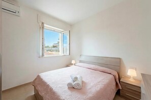 A hotel room with a bed, a nightstand with a lamp, a window with a view, and an air conditioning unit.