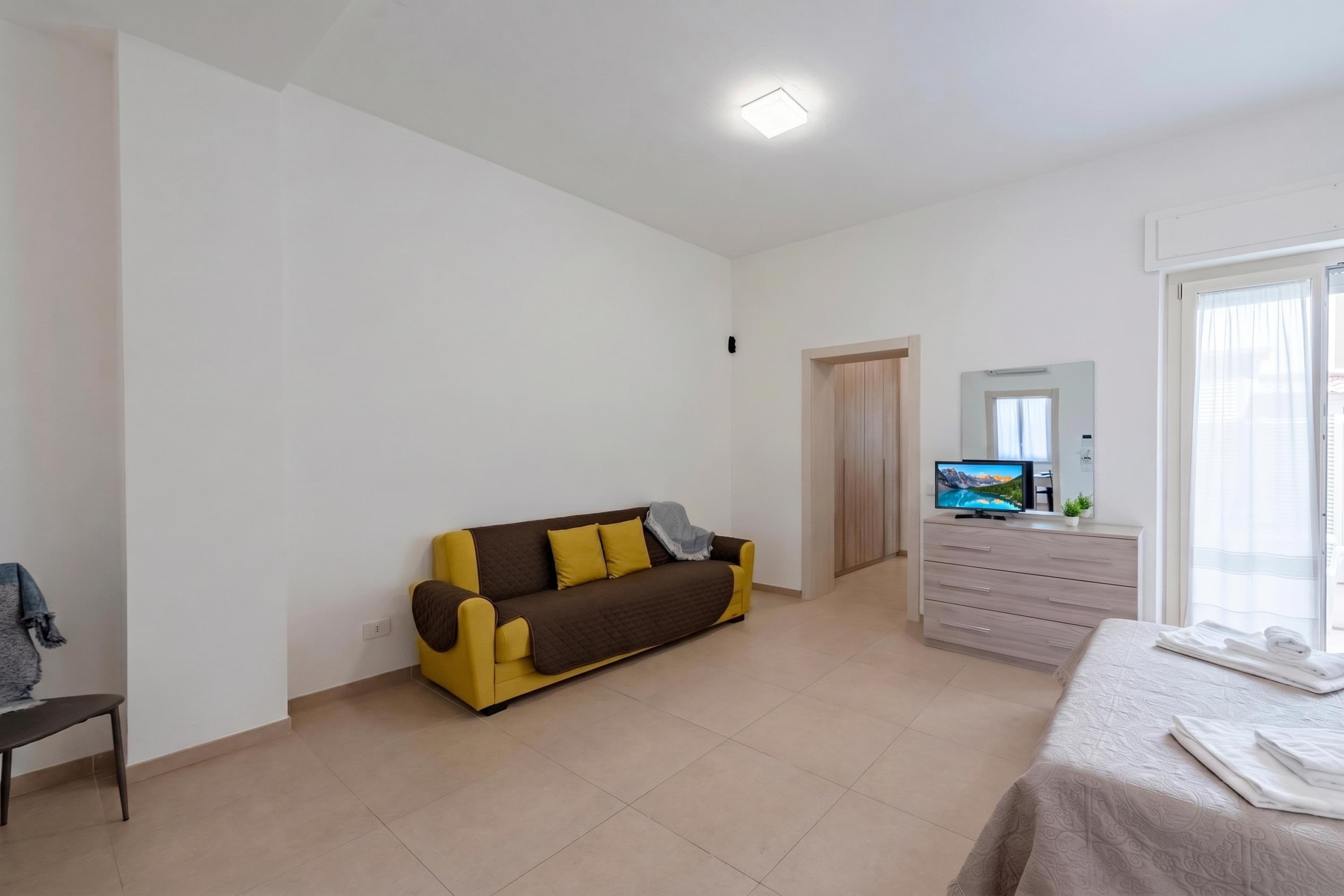 A modern, well-lit room with a sofa, a bed, a TV, and a dresser.