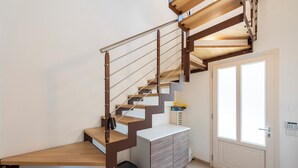 A staircase with wooden steps and metal railings, leading to a landing with a white cabinet and a door with glass panels. - Suite Ondina Viareggio Apartments (Viareggio)