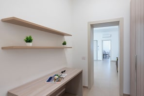 A modern hallway with a wooden desk, two potted plants, and a view into a dining area. - Suite Ondina Viareggio Apartments (Viareggio)
