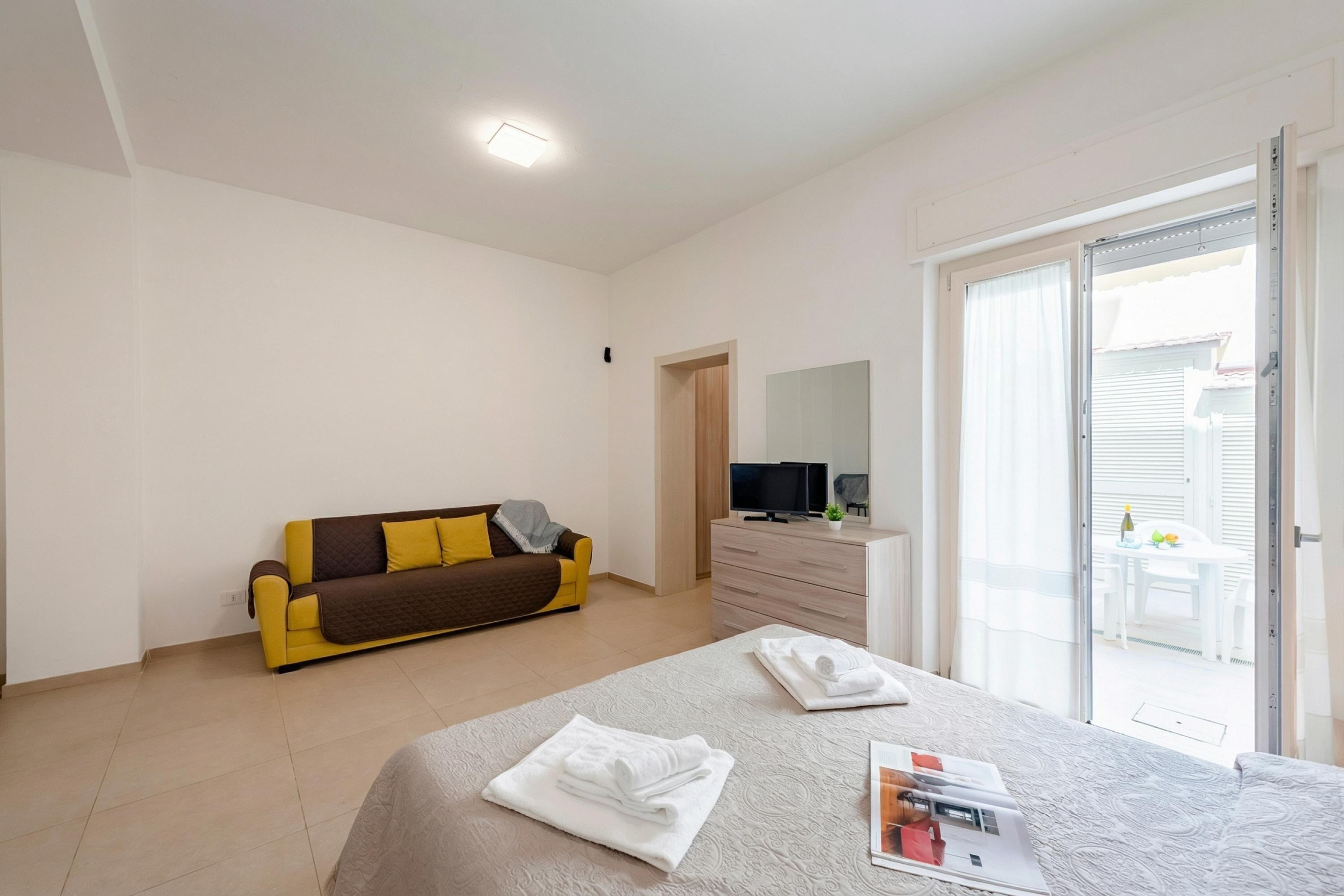 A hotel room with a bed, a sofa, a TV, and a balcony.