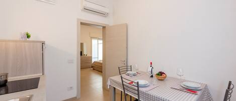 A modern kitchen with a dining area. There is a table set with plates, glasses, and a bowl of fruit.