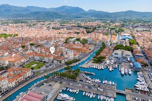A marina with numerous boats docked, surrounded by a cityscape with red-roofed buildings and a clear view of distant mountains.