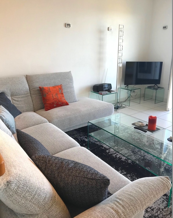 Un salon moderne avec un canapé d’angle, une table basse en verre et un téléviseur à écran plat.