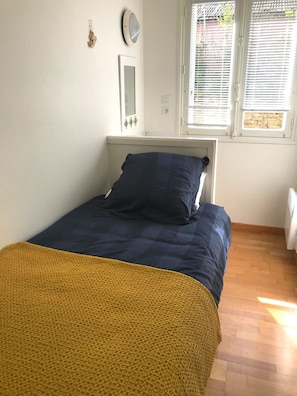 Une chambre à coucher avec un lit, une fenêtre avec des stores, un luminaire fixé au mur et un radiateur.