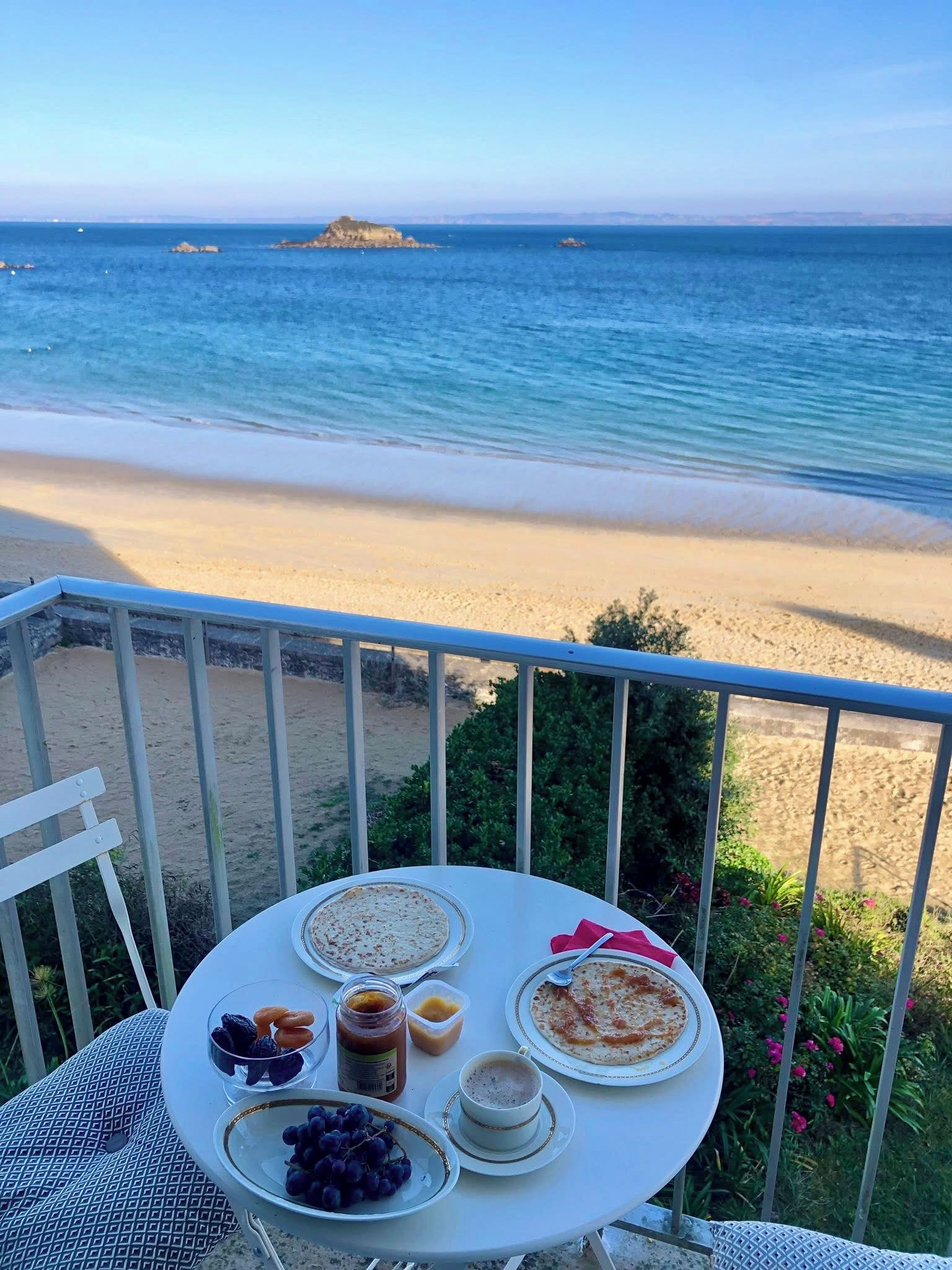 A table with food and drinks on a balcony overlooking a beach with clear skies.