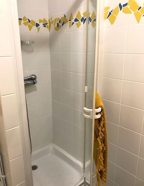 Chuveiro com porta de vidro, azulejos brancos e uma toalha amarela pendurada na maçaneta.