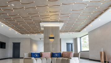 Een moderne lobby met een gebogen bank, een centrale pilaar en een plafond met lineaire verlichtingsarmaturen.