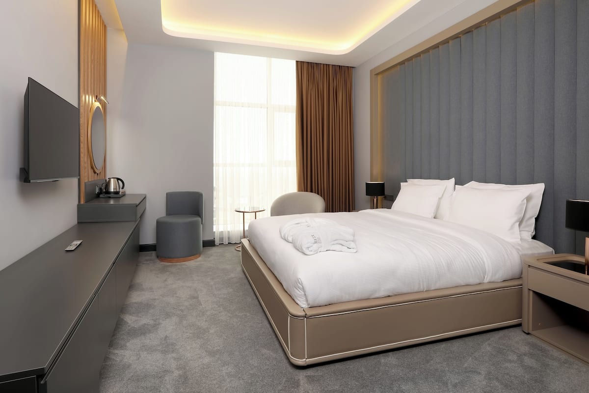 A modern hotel room with a large bed, a flat-screen TV, a small desk, and a seating area.