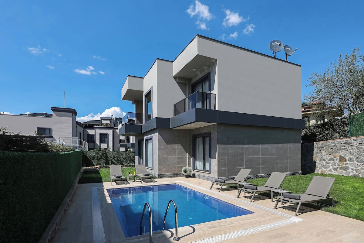 A modern two-story house with a swimming pool, outdoor seating, and a stone wall.