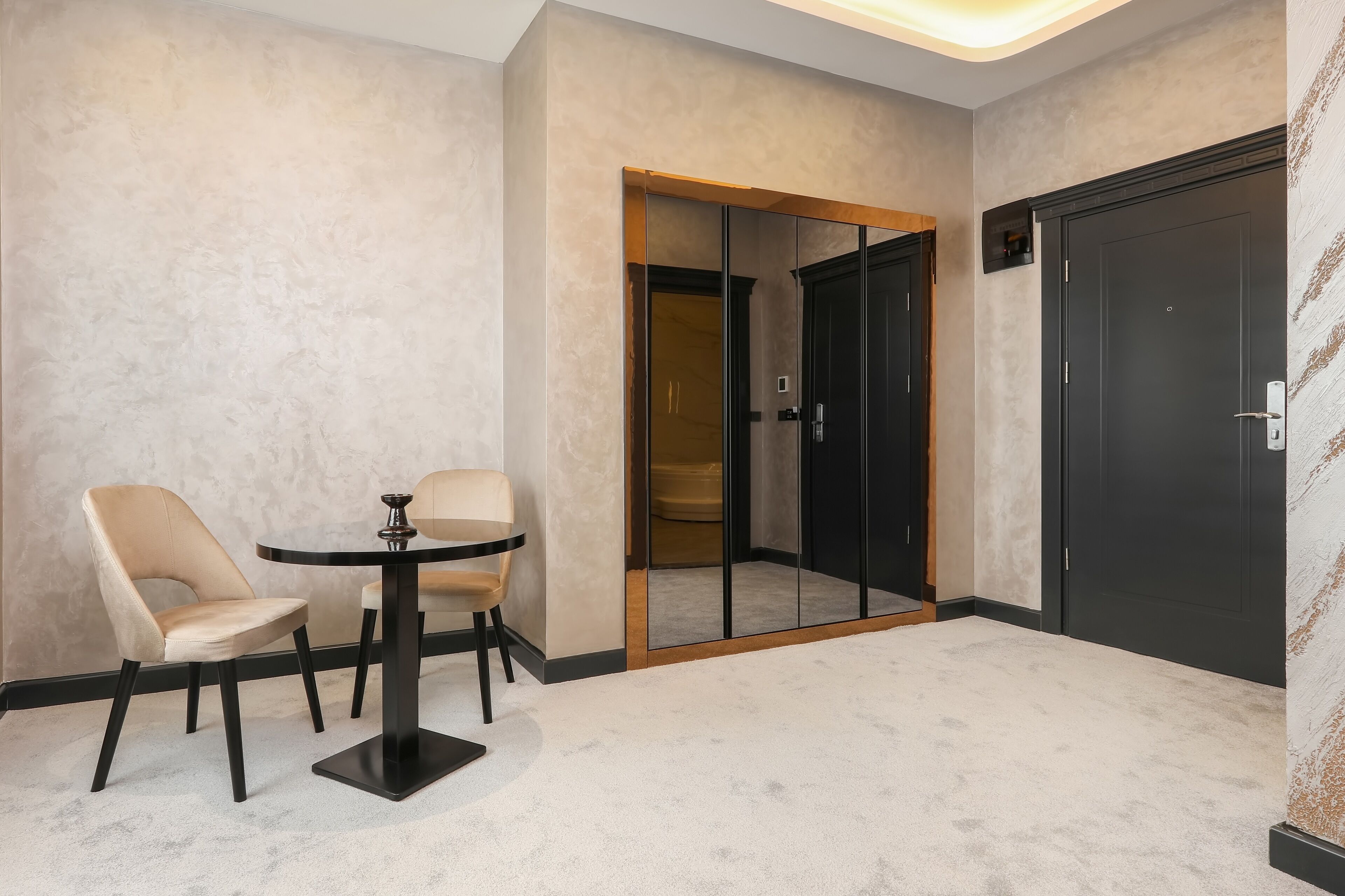 A room with a round table and two chairs, a black door, and a mirrored closet.