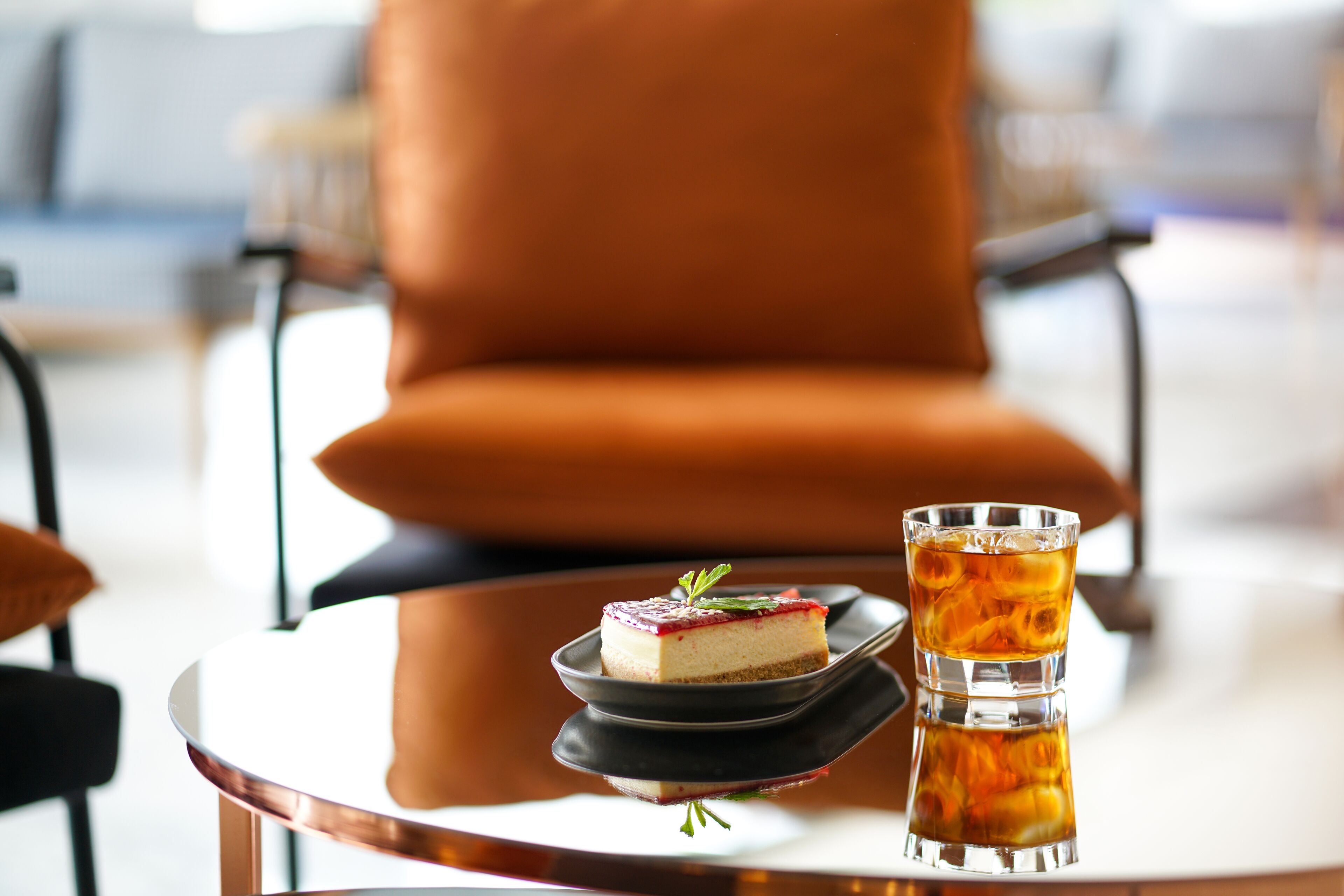 Een toetje op een bord met een glas ijsthee op een tafel in een kamer met een grote oranje fauteuil.