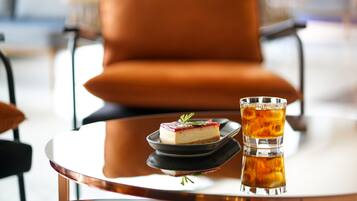 Een toetje op een bord met een glas ijsthee op een tafel in een kamer met een grote oranje fauteuil.