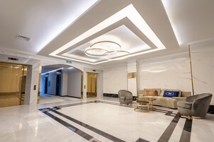Un vestíbulo moderno con piso de mármol, una mesa de recepción y un área de descanso con sofás y sillones.