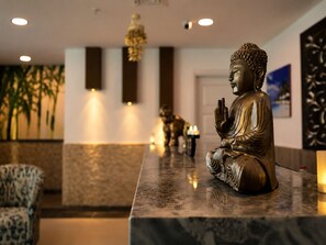 Una estatua de Buda sobre un mostrador de mármol en un vestíbulo con diseño moderno, que incluye una silla estampada y un muro decorativo.