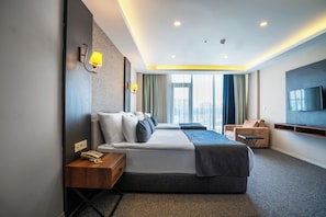 A modern hotel room with a large bed, bedside lamps, a desk, a chair, and a TV mounted on the wall.