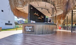 A snack bar with a wooden counter, hanging decorations, and a view of the hotel in the background. - Lavia Hotels Lara  (Antalya)