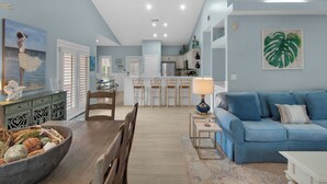 A spacious living area with a blue sofa, a dining table with chairs, and a kitchen in the background.