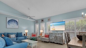 A living room with a blue sofa, a coffee table, a TV, and a dining table with chairs.