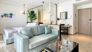 Une chambre d’hôtel moderne avec un lit, un canapé bleu clair, une table basse en marbre et un grand miroir.